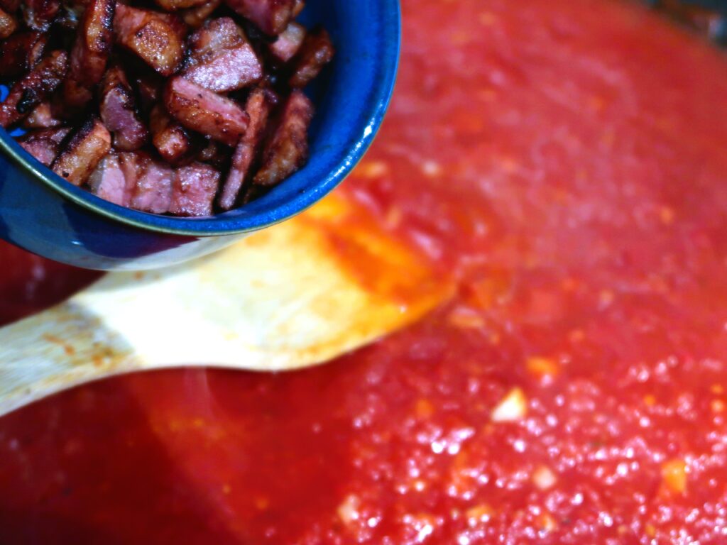 adding the cooked pancetta to the sauce